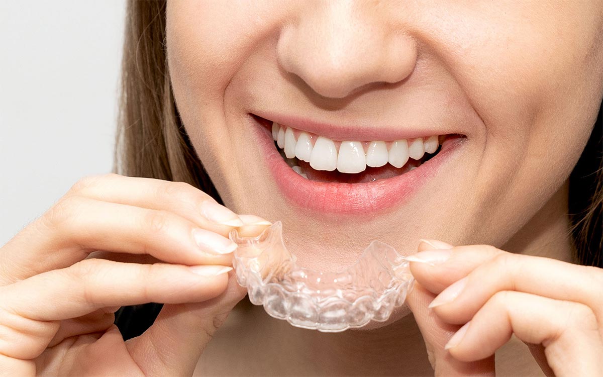 Mund zeigt einen lächelnden Mund, davor zwei Hönde die eine Schiene halten